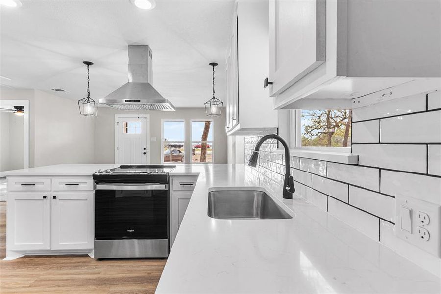 Kitchen featuring stainless steel range with electric cooktop, white cabinets, island range hood, a peninsula, and hanging light fixtures