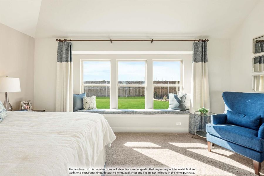 Bedroom with large triple window seat, vaulted ceiling, carpet flooring, and blue accent chair overlooking backyard