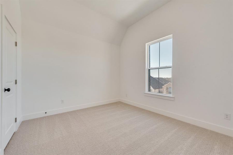 Empty room with light colored carpet and lofted ceiling Empty room with light colored carpet and lofted ceiling