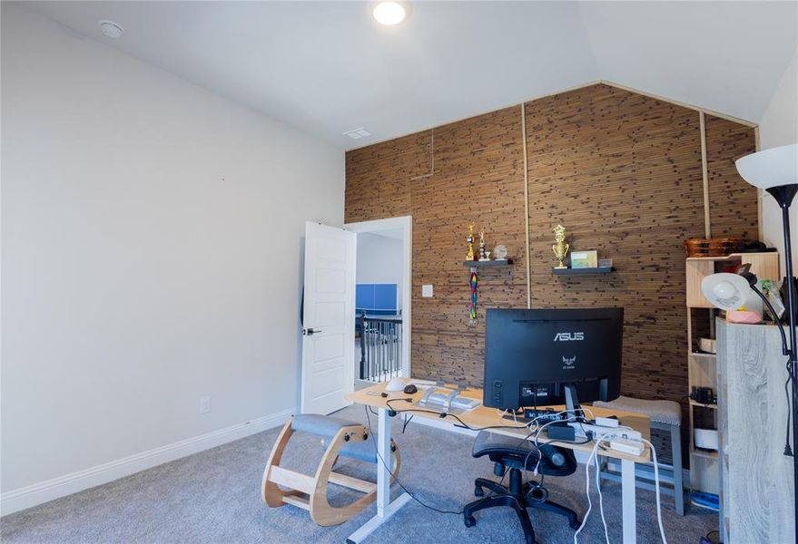 Office space with lofted ceiling, carpet flooring, and an accent wall