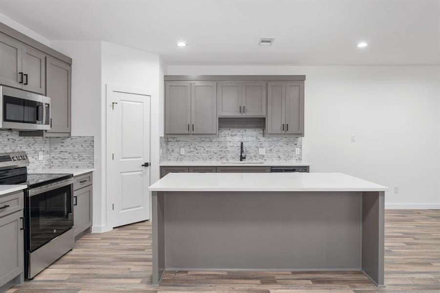 Kitchen with gray cabinets, appliances with stainless steel finishes, and a center island