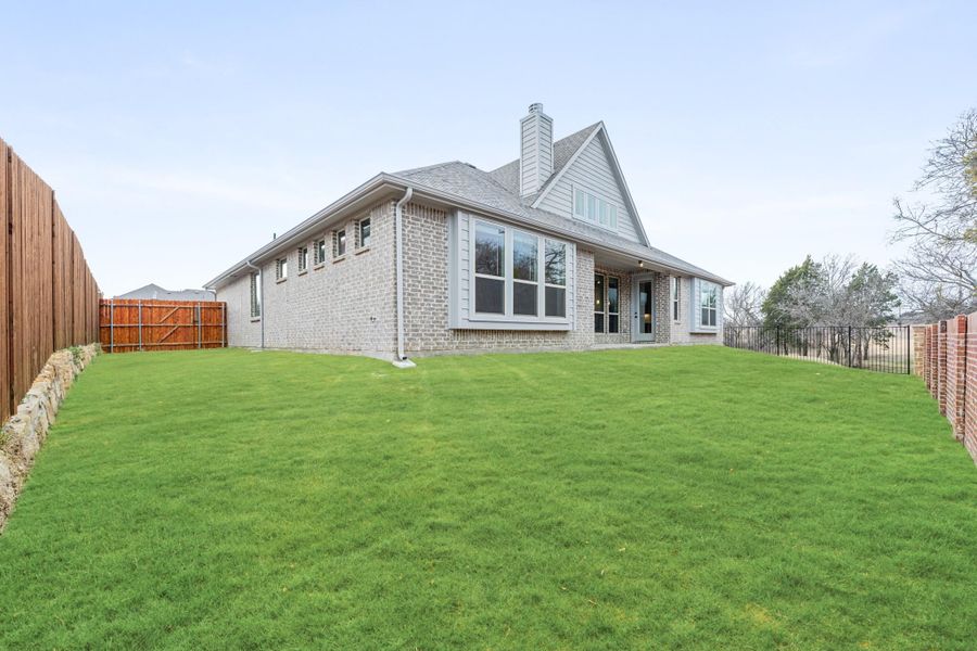 Rear exterior of brick home with large green lawn, wood fence, and multiple windows Rear exterior of brick home with large green lawn, wood fence, and multiple windows