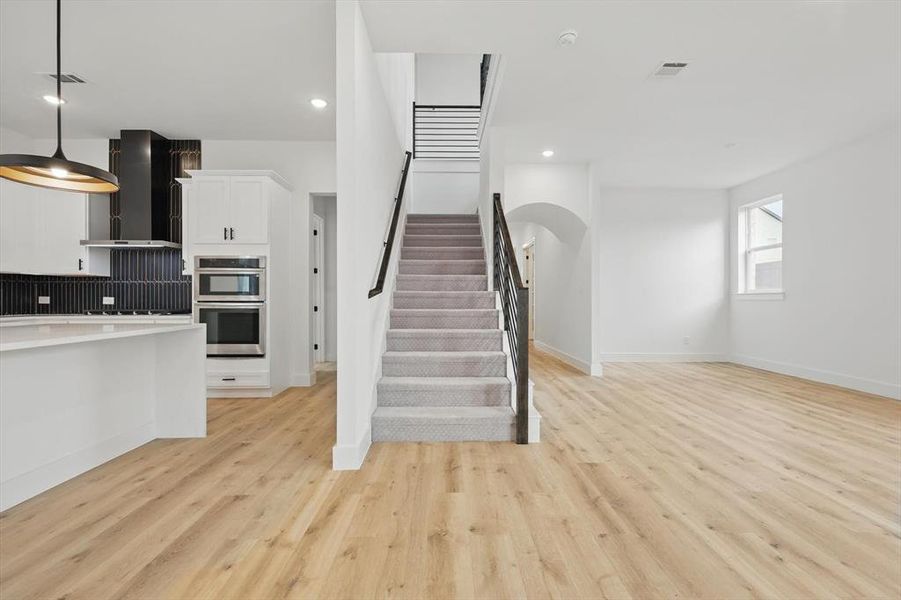 Kitchen featuring wall chimney exhaust hood, stainless steel double oven, light wood-type flooring, white cabinets, and baseboards