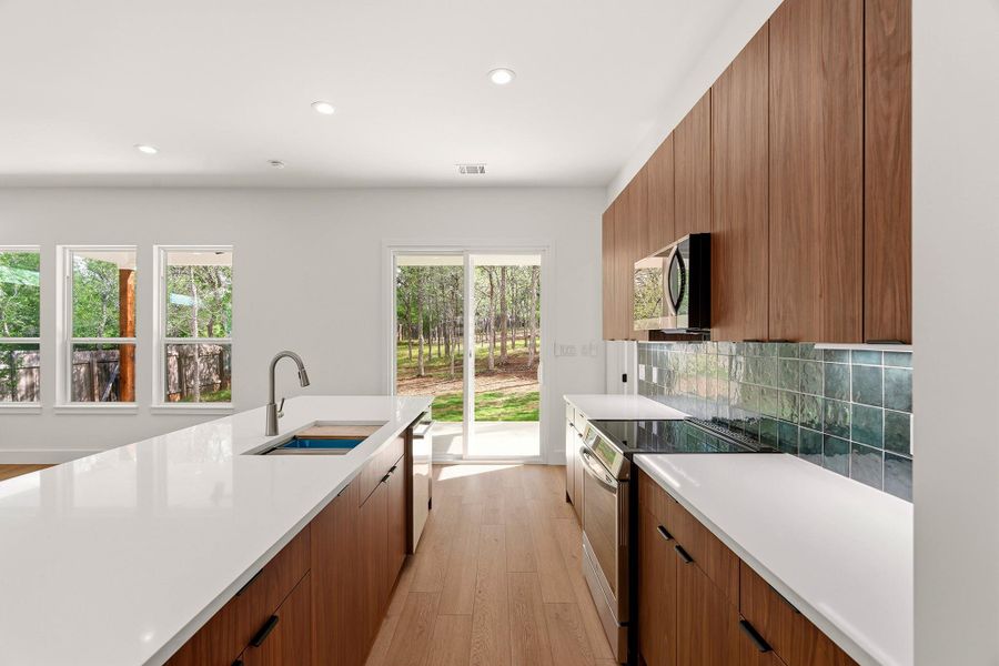 Dual tone kitchen featuring modern cabinets, stainless steel appliances, light wood-style flooring, recessed lighting, and light stone countertops