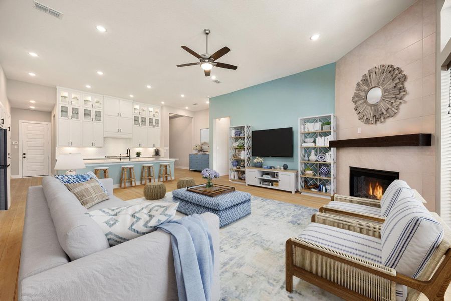 This inviting open-concept living area showcases soaring ceilings, recessed lighting, and a cozy fireplace framed by modern tile and a sleek wood mantel. Large windows bring in abundant natural light, enhancing the airy atmosphere. The seamless flow into the bright kitchen, featuring extensive cabinetry and a spacious island, creates the perfect setting for both entertaining and everyday living.