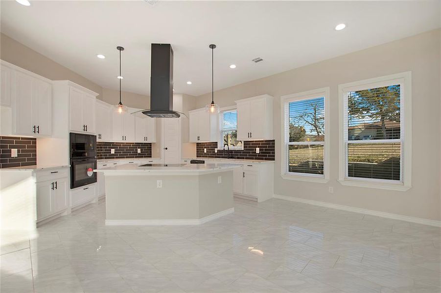 Kitchen featuring island range hood, decorative light fixtures, white cabinetry, decorative backsplash, and a center island