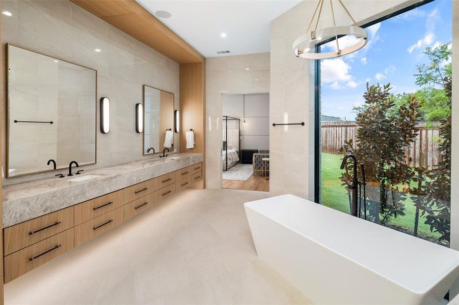 Spa-inspired primary bathroom featuring a freestanding soaking tub perfectly positioned to enjoy views of the private yard. Upgraded floor-to-ceiling tile walls, a floating vanity with under-cabinet lighting, and elegant designer fixtures create a luxurious and serene retreat.