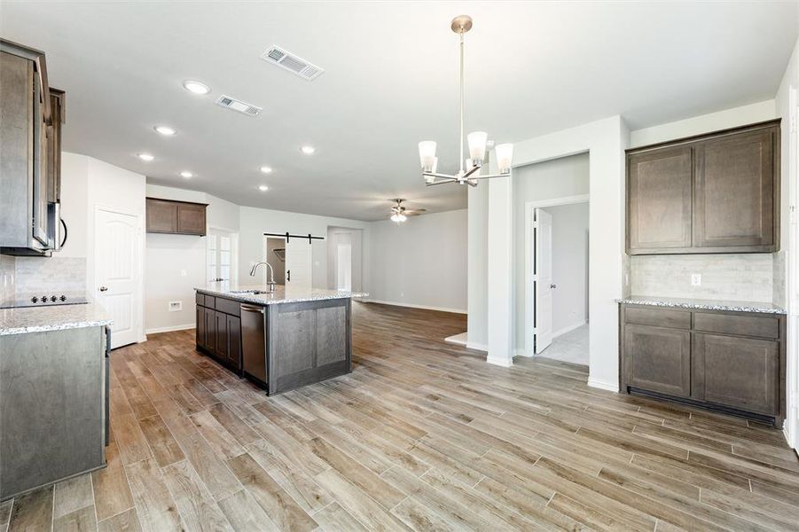 Kitchen with decorative backsplash, a barn door, a chandelier, an island with sink, and dark brown cabinets