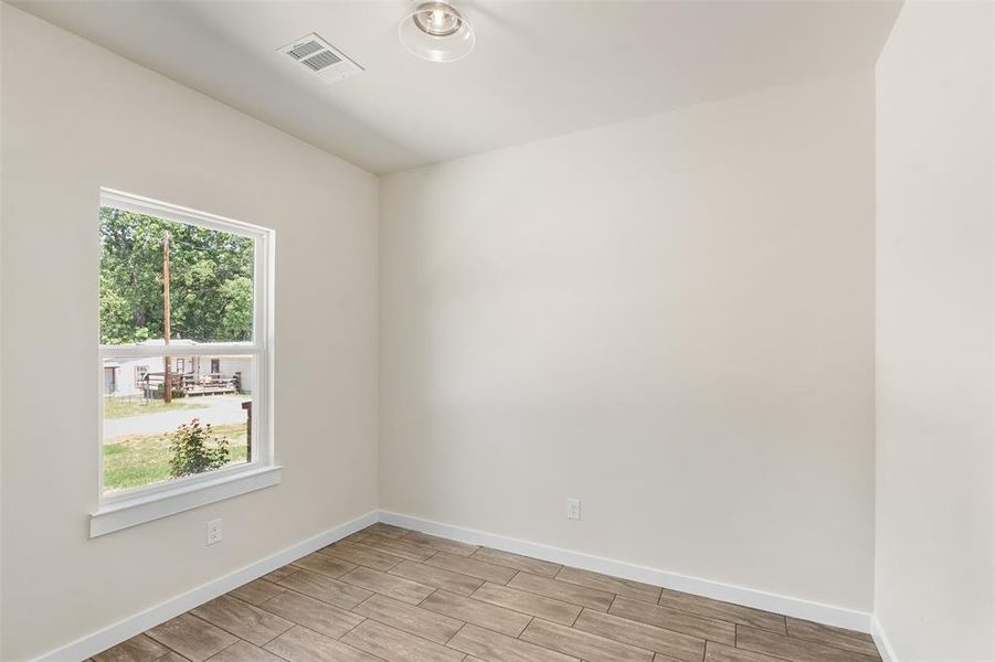 Room featuring wood-finish flooring, a single window with white trim, and a flush-mount ceiling light fixture Room featuring wood-finish flooring, a single window with white trim, and a flush-mount ceiling light fixture