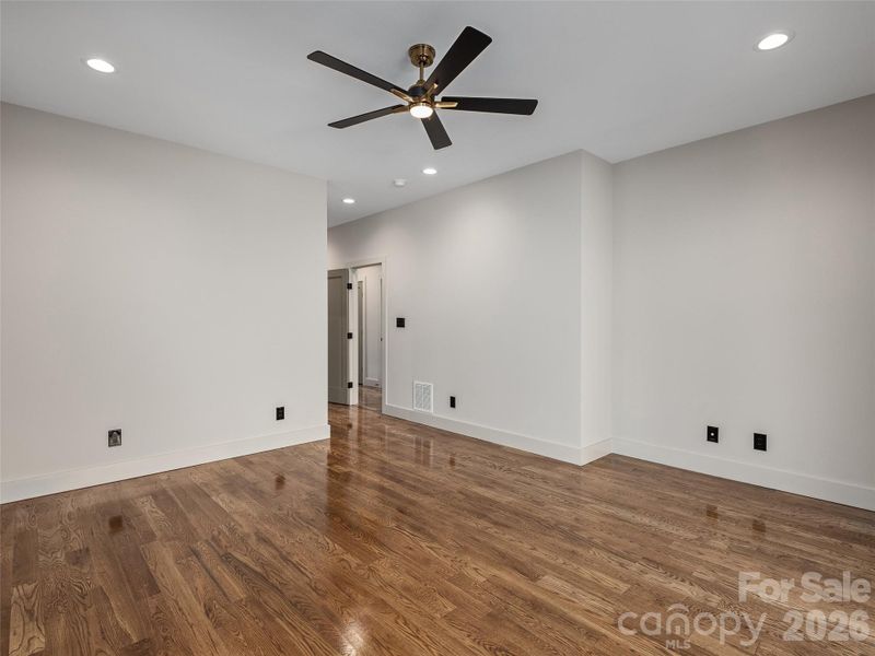 Another view of the primary bedroom showcasing generous proportions, oak hardwood floors, recessed lighting, and clean contemporary finishes.
