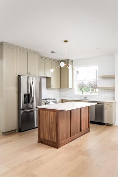 Kitchen featuring stainless steel appliances, light wood-style floors, a center island, decorative light fixtures, and backsplash