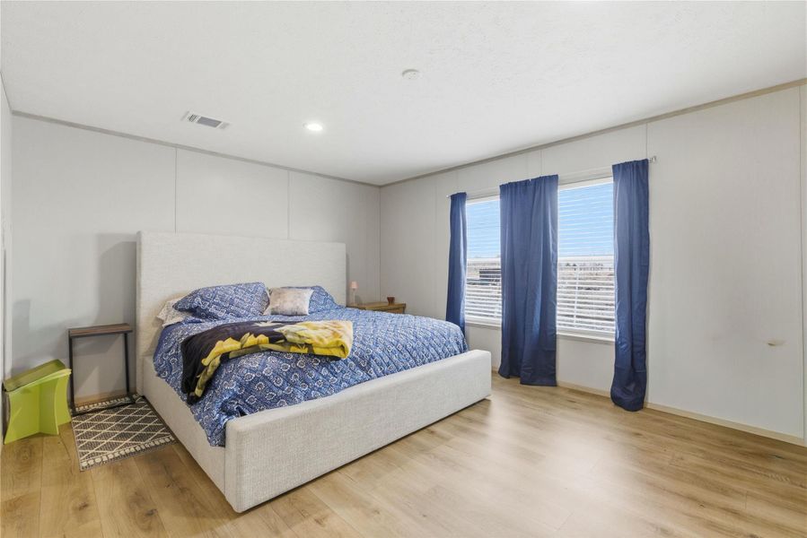 A well-lit bedroom features durable hardwood flooring and large windows with privacy blinds, offering ample natural illumination.