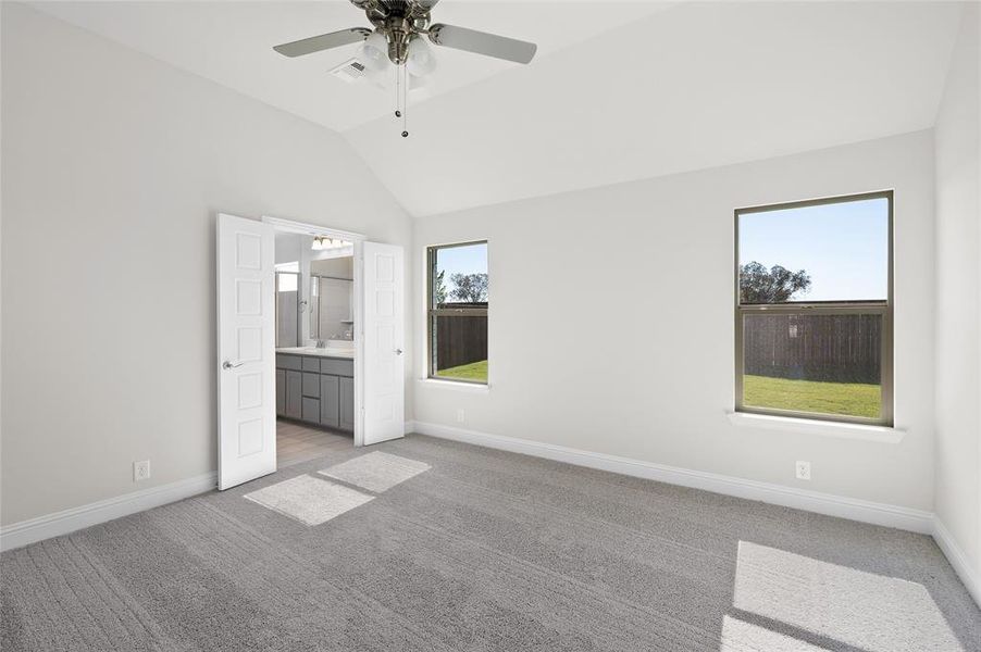 Unfurnished bedroom featuring carpet flooring, vaulted ceiling, ensuite bath, and a ceiling fan