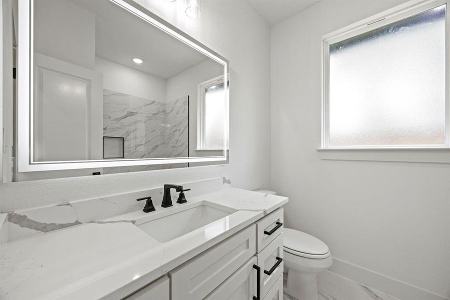 Bathroom featuring marble look tiles, vanity, toilet, baseboards, and a marble finish shower Bathroom featuring marble look tiles, vanity, toilet, baseboards, and a marble finish shower