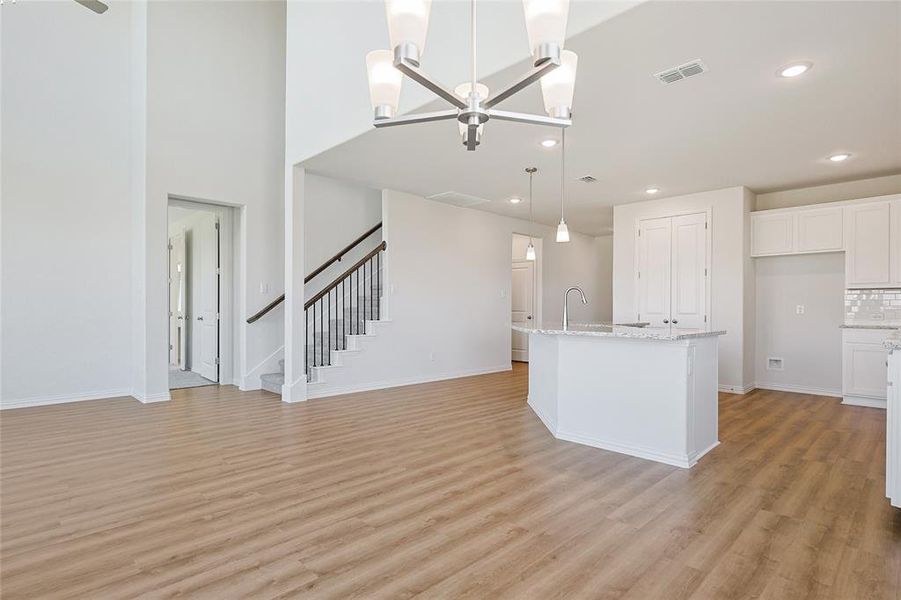 Kitchen with white cabinets, pendant lighting, a kitchen island with sink, a chandelier, and light wood-type flooring