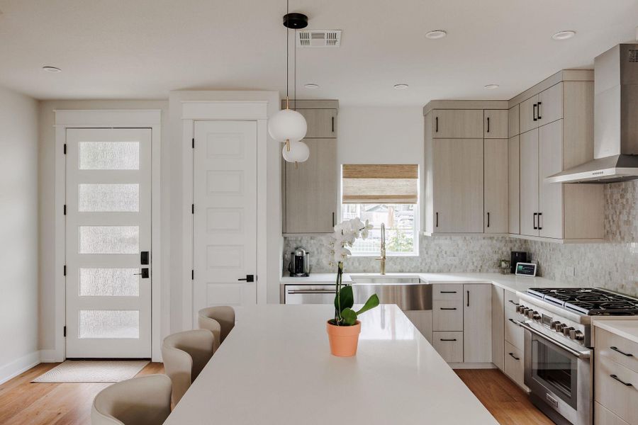 Kitchen featuring stainless steel appliances, light wood finish cabinetry, light wood finished floors, hanging light fixtures, and decorative backsplash