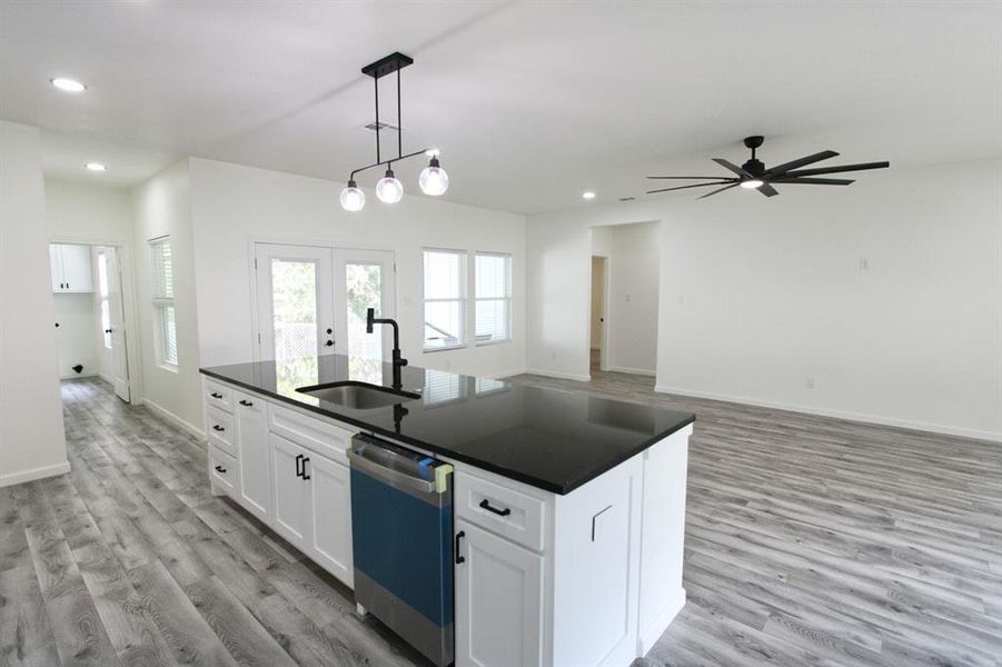 Kitchen with white cabinets, hanging light fixtures, open floor plan, dishwashing machine, and french doors Kitchen with white cabinets, hanging light fixtures, open floor plan, dishwashing machine, and french doors