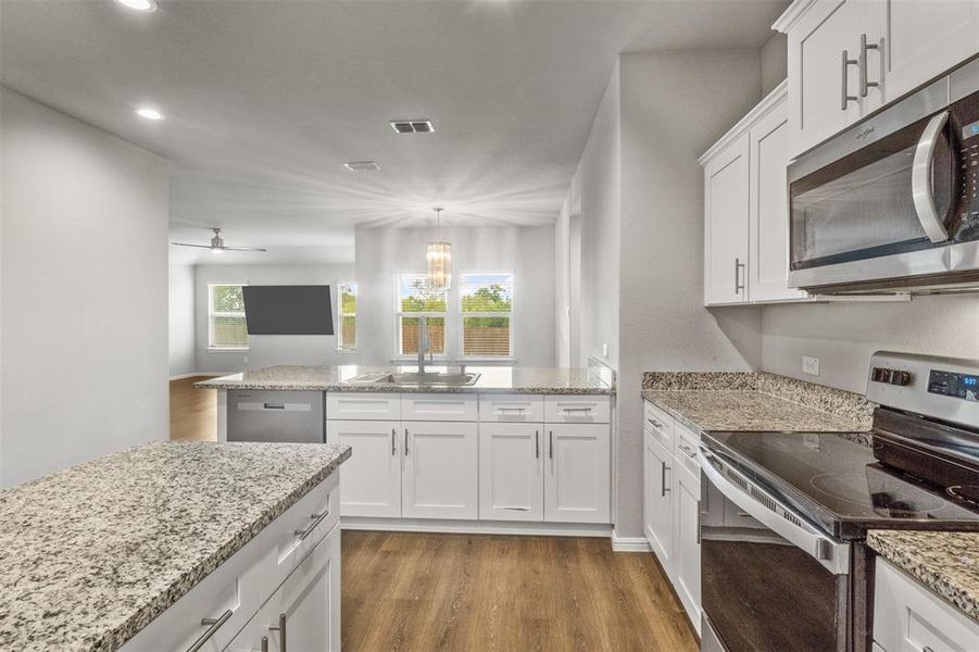 Kitchen with white cabinets, appliances with stainless steel finishes, light hardwood / wood-style floors, and a healthy amount of sunlight