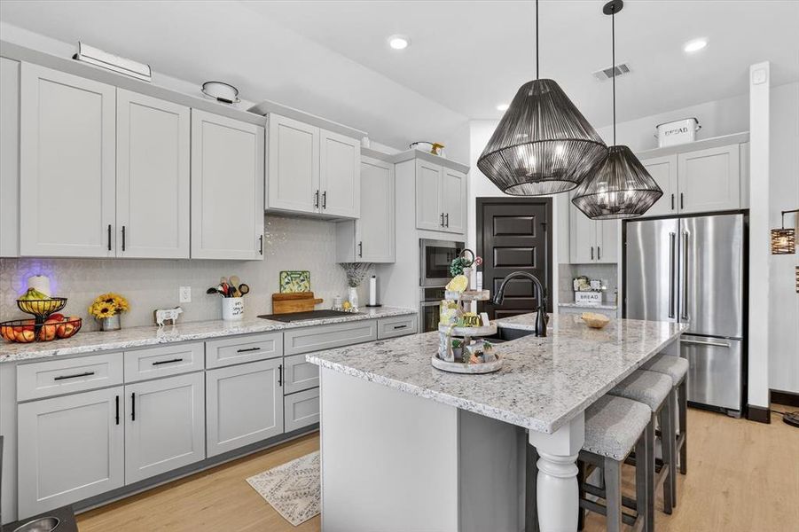 Modern kitchen featuring light gray cabinetry, light-toned wood-finish flooring, and a large central island with a light-colored countertop