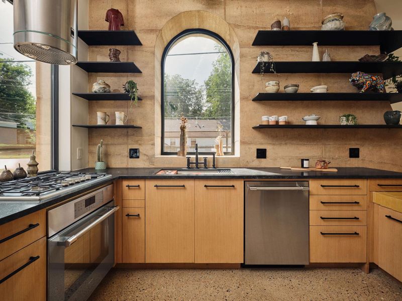 Kitchen featuring open custom steel shelves, stainless steel appliances, dark countertops, decorative backsplash, and aggregate flooring Kitchen featuring open custom steel shelves, stainless steel appliances, dark countertops, decorative backsplash, and aggregate flooring