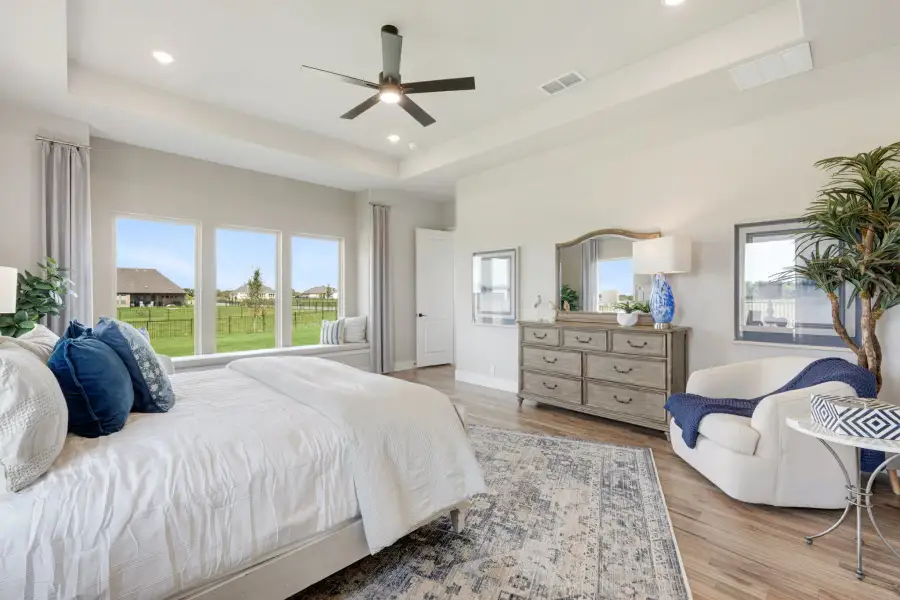 Master bedroom with hardwood floors, ceiling fan, large windows, and wood dresser with mirror Master bedroom with hardwood floors, ceiling fan, large windows, and wood dresser with mirror