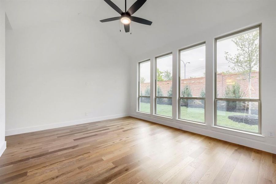 This room features hardwood flooring, a vaulted ceiling with a modern ceiling fan, and a wall of four large windows