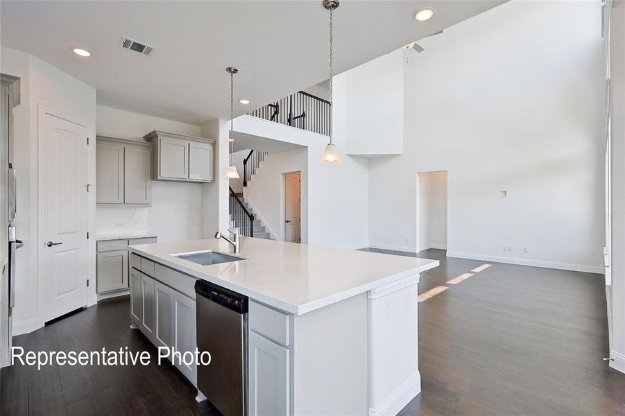 Open-concept living space featuring high ceilings, dark wood-finish flooring, and a kitchen island with a built-in sink and stainless steel dishwasher