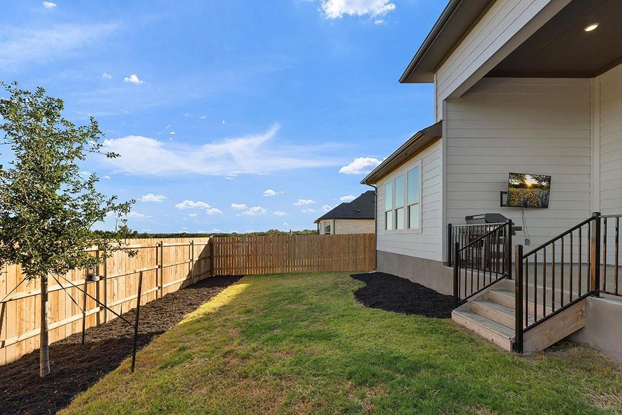 A wooden privacy fence surrounds a grassy yard bordering the covered back patio.