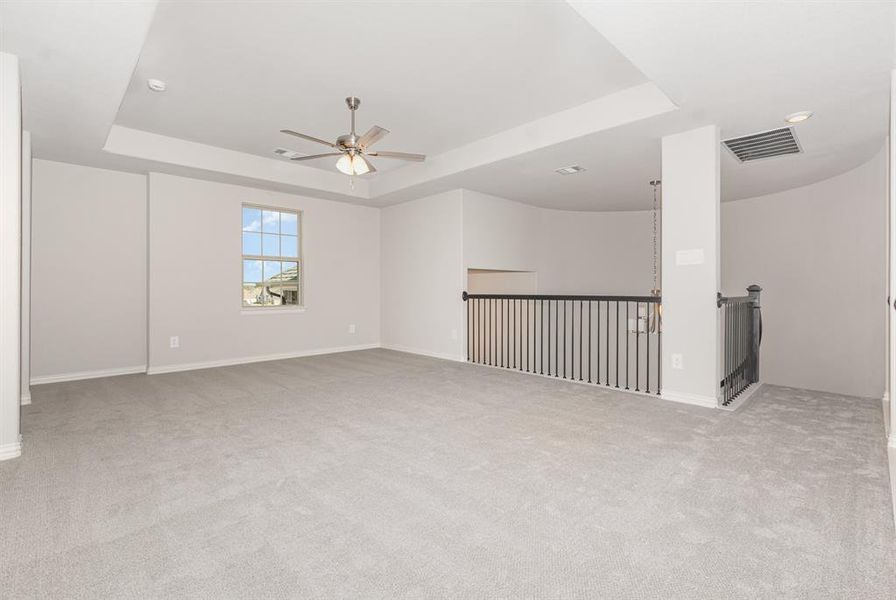 Empty room with a tray ceiling, light colored carpet, and a ceiling fan