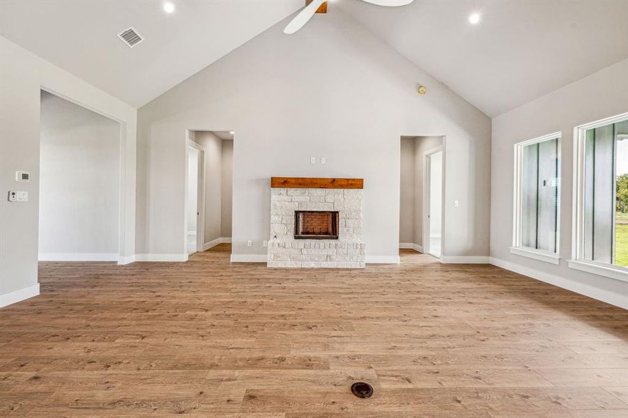 Unfurnished living room featuring a fireplace, light hardwood / wood-style flooring, high vaulted ceiling, and ceiling fan