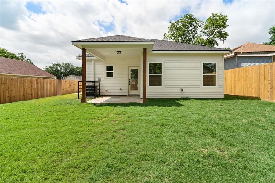Expansive backyard featuring a manicured lawn and a covered patio with wood support beams