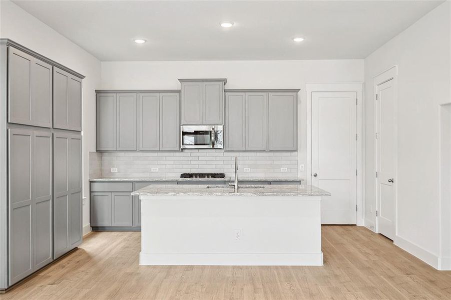 Kitchen featuring gray cabinetry, light hardwood / wood-style flooring, light stone countertops, and an island with sink