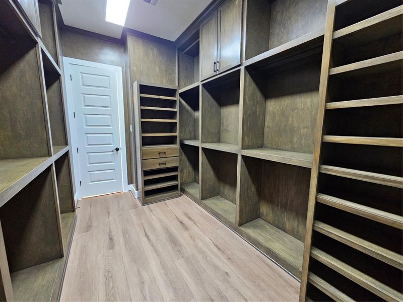 This photo shows a spacious walk-in closet with ample wooden shelving and storage compartments, featuring a modern design and light wood flooring.