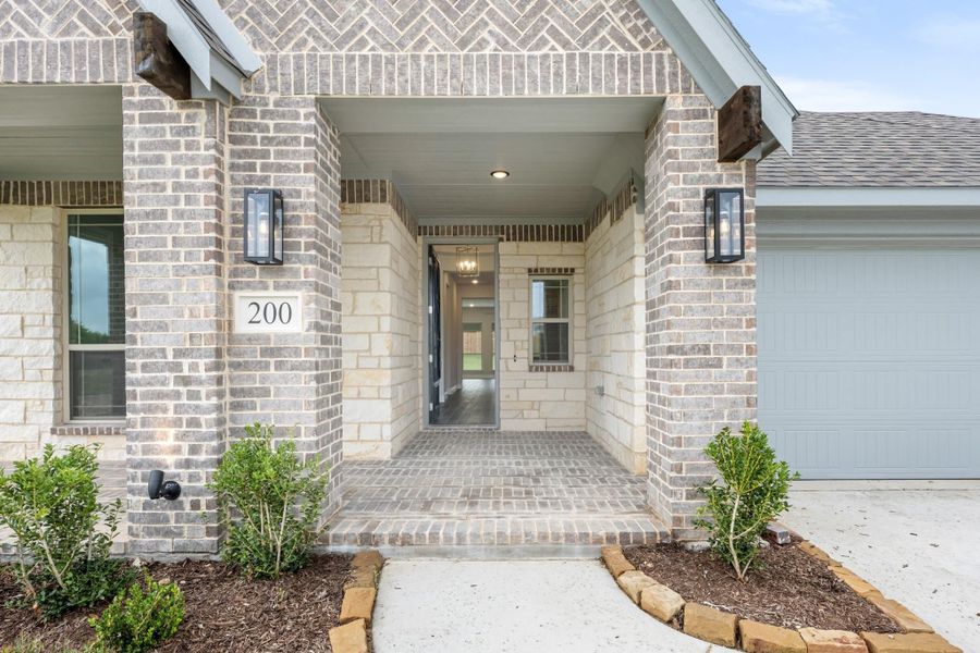 Covered front entry of brick home with address number 200, wall sconces, and attached garage nearby.