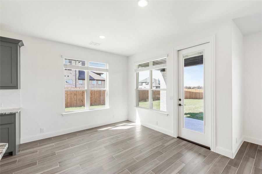 Bright dining area with wood-look tile floors, two windows, and a glass back door overlooking a fenced yard Bright dining area with wood-look tile floors, two windows, and a glass back door overlooking a fenced yard