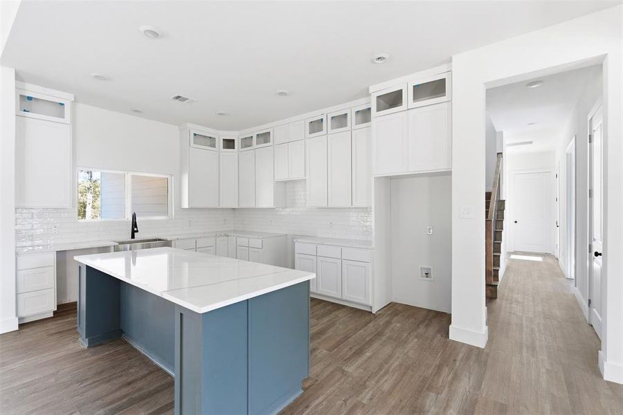 Kitchen with white cabinets, a kitchen island, wood finished floors, and backsplash Kitchen with white cabinets, a kitchen island, wood finished floors, and backsplash