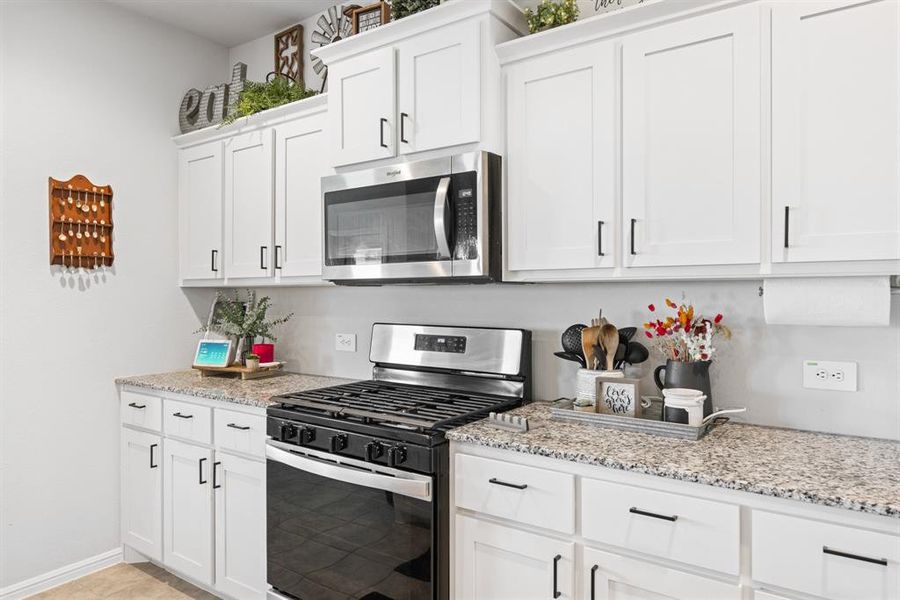 Kitchen with stainless steel appliances, white cabinetry, and light stone counters