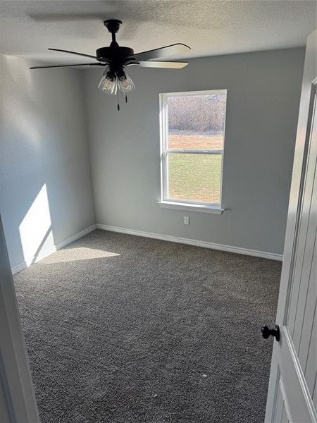 Carpeted empty room with ceiling fan and a textured ceiling