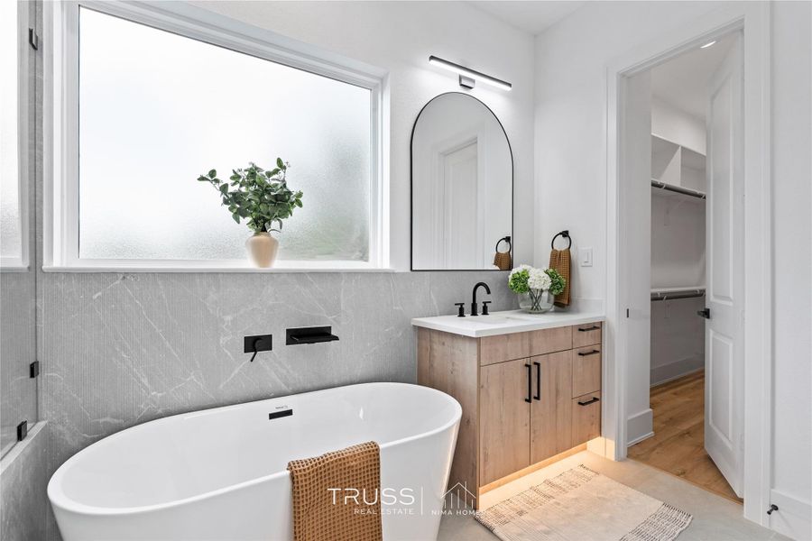 The spa-like ensuite exudes quiet luxury, featuring dual vanities framed in warm wood tones and a statement freestanding tub.