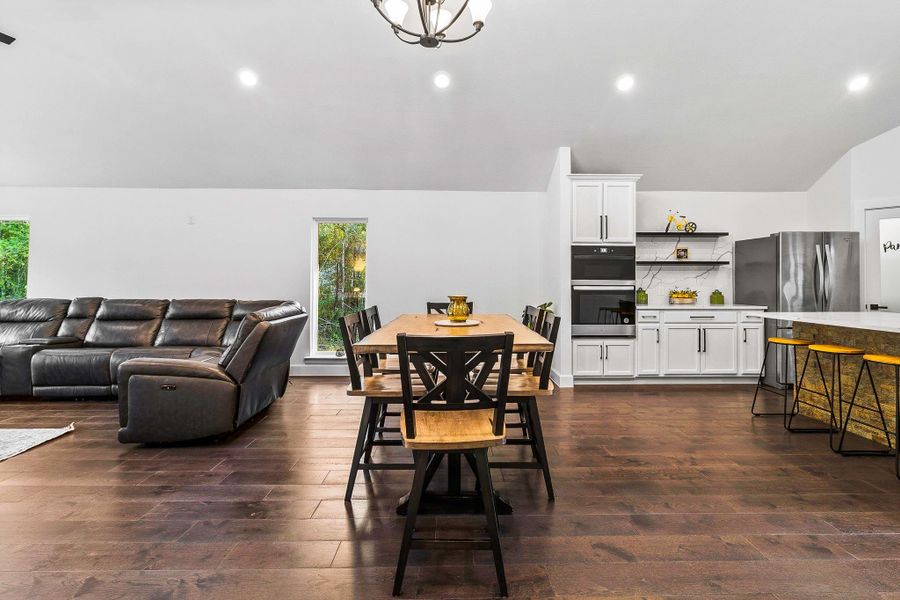 This open-concept living area features sleek hardwood floors, a modern kitchen with white cabinetry, stainless steel appliances, and a cozy dining area. A spacious leather sectional complements the bright, airy space, ideal for entertaining.