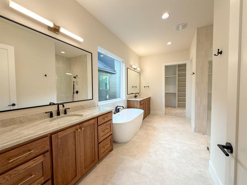 Spacious bathroom featuring dual wood vanities with undermount sinks and stone countertops, a freestanding tub, a large walk-in shower with clear glass enclosure, and tile flooring