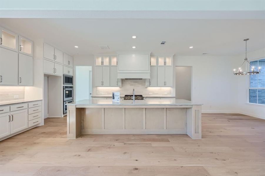 Kitchen with appliances with stainless steel finishes, light hardwood / wood-style flooring, tasteful backsplash, and an island with sink