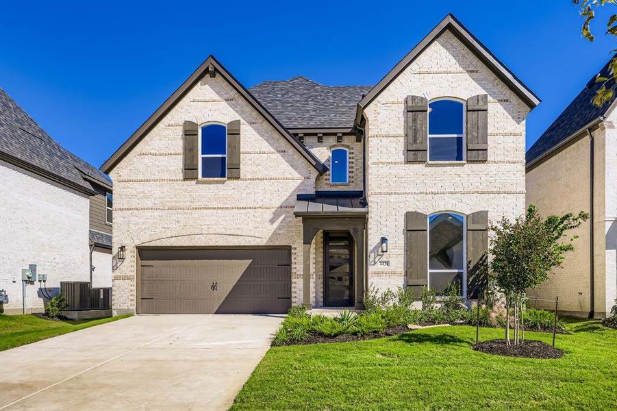 French provincial home featuring brick siding, concrete driveway, a front yard, and an attached garage