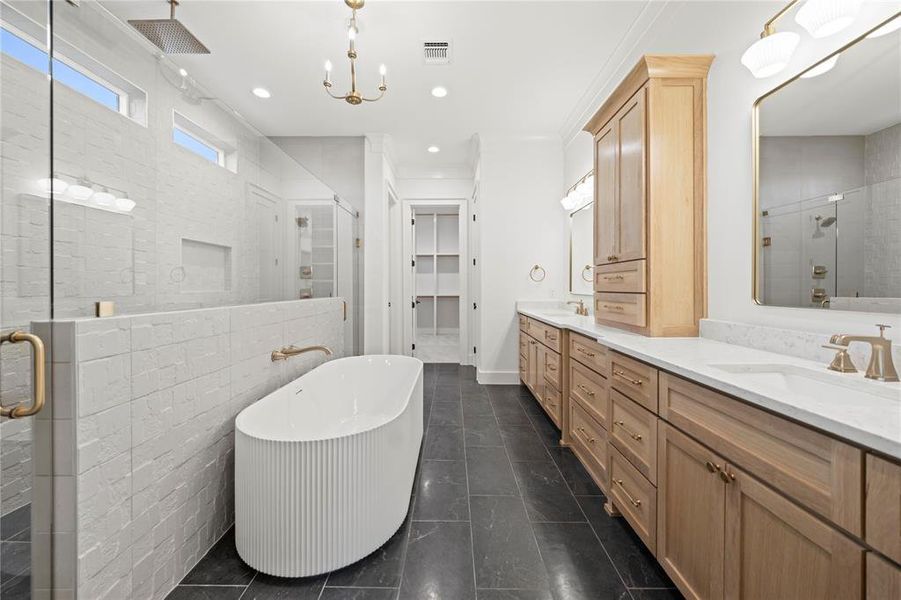 Spacious bathroom featuring a fluted freestanding tub, a large walk-in shower with a rain showerhead, a dual vanity with light-tone wood cabinetry, and dark tile flooring