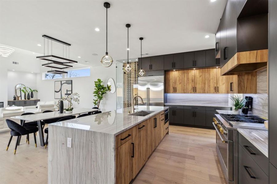 Kitchen featuring a spacious island, sink, high end appliances, hanging light fixtures, and light stone countertops