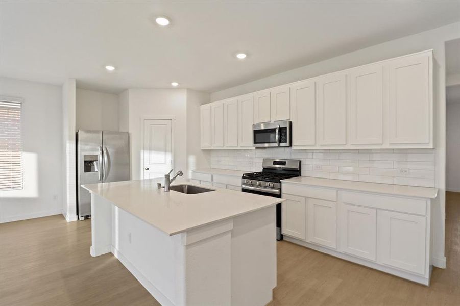 Kitchen with white cabinetry, stainless steel appliances, a kitchen island with sink, light wood-style floors, and recessed lighting