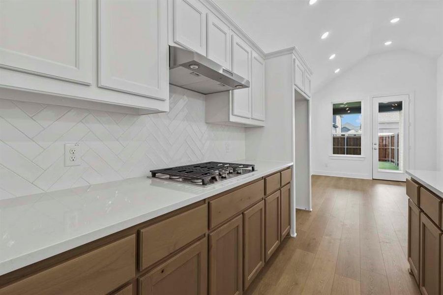 Kitchen featuring light wood-style floors, vaulted ceiling, under cabinet range hood, backsplash, and recessed lighting Kitchen featuring light wood-style floors, vaulted ceiling, under cabinet range hood, backsplash, and recessed lighting