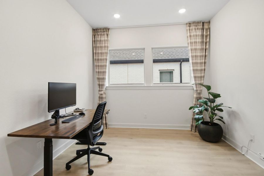 Bright and inviting home office featuring a sleek wooden desk, comfortable chair, and large windows with plaid curtains, complemented by light wood flooring and a vibrant potted plant.