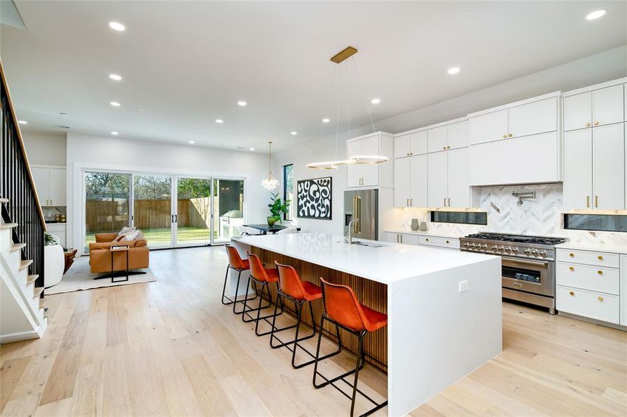 Kitchen featuring pendant lighting, high end appliances, white cabinets, an island with sink, and a kitchen bar