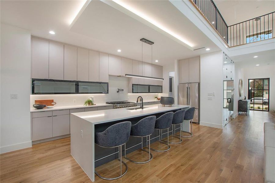 Kitchen featuring stainless steel refrigerator, modern cabinets, a breakfast bar area, recessed lighting, and a towering ceiling Kitchen featuring stainless steel refrigerator, modern cabinets, a breakfast bar area, recessed lighting, and a towering ceiling